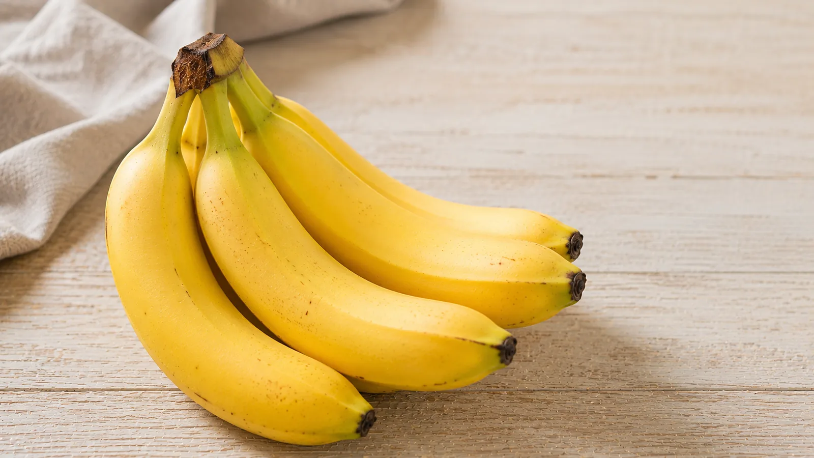 Mehrere reife gelbe Bananen als Bund auf hellem Holzuntergrund